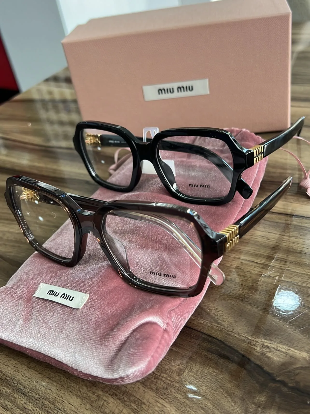Deux montures de vue Miu Miu posées sur leur pochette rose, dans la boutique